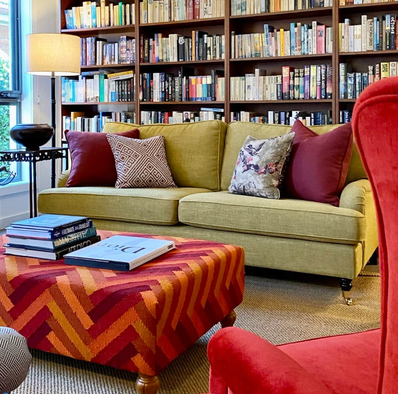 Colourful library living room with green sofa, red accents and patterned ottoman styled by Gabriel Jacka